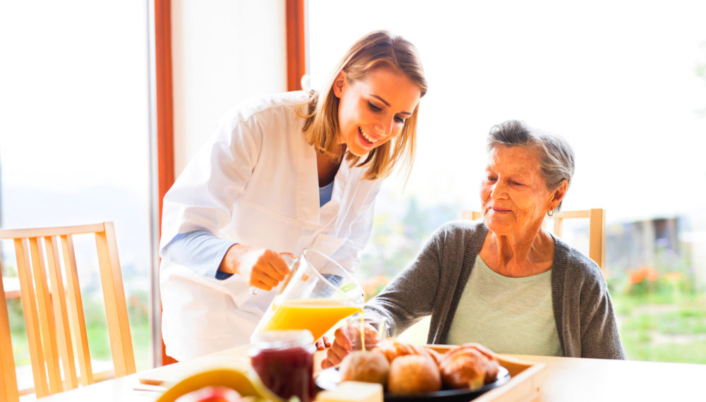 caregiver pouring juice for old lady